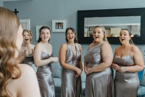 Bridesmaids in silver satin dresses share a joyful moment of laughter while getting ready for the wedding ceremony.