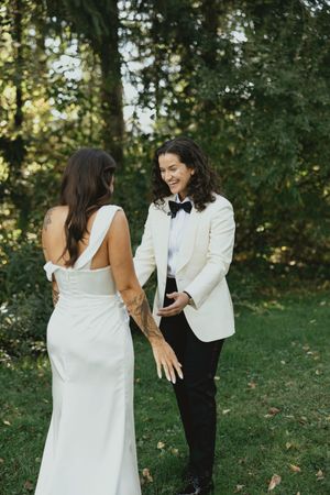 Two people in wedding attire share a joyful moment together outdoors with trees and greenery in the background.