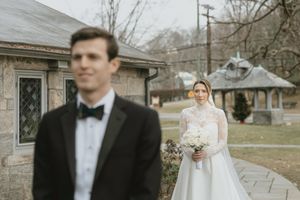 A wedding couple walks together outdoors during a winter day with bare trees in the background.