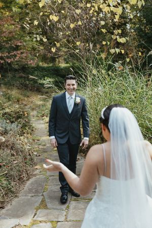 A wedding couple takes photos on a stone pathway surrounded by autumn foliage.