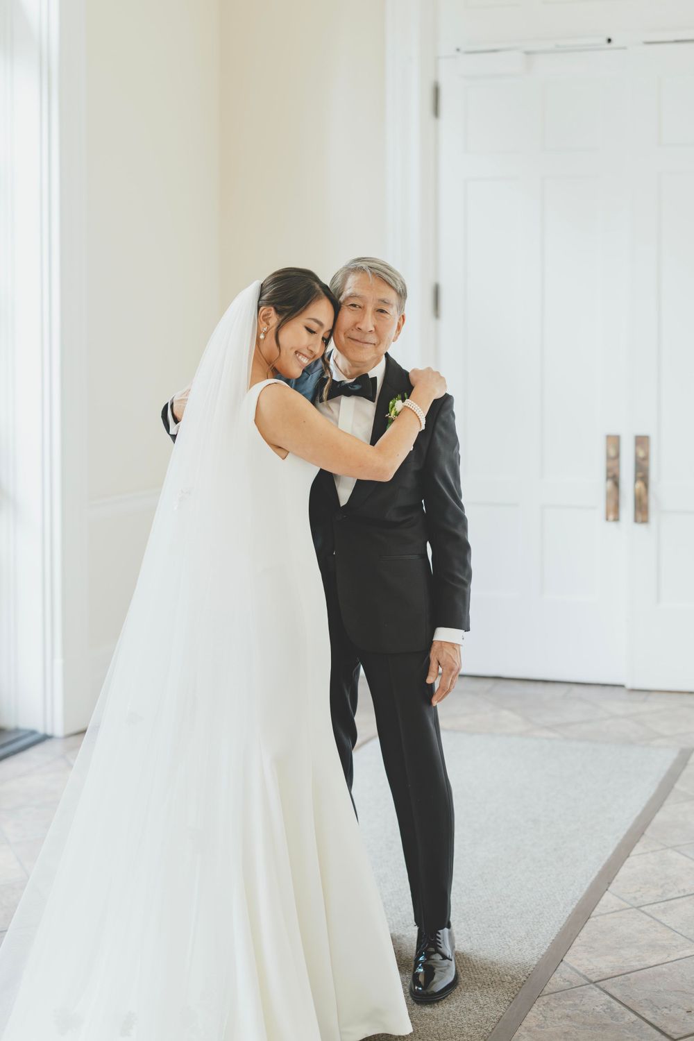 A tender moment between a bride in a white gown and an older gentleman in a black tuxedo at a formal wedding.