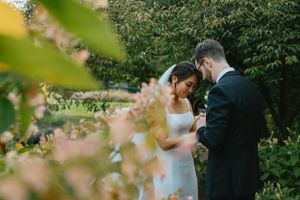 A couple shares an intimate moment in a garden with soft pink flowers in the foreground.