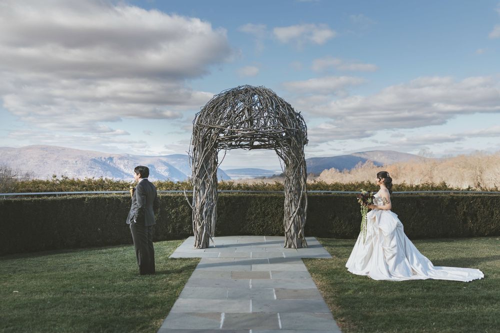 Elegant outdoor wedding ceremony setup with mountain views and rustic wooden arch decorated with flowing white fabric.