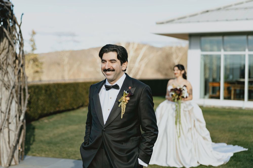 Elegant outdoor wedding scene with couple walking through a rustic venue on a sunny autumn day.