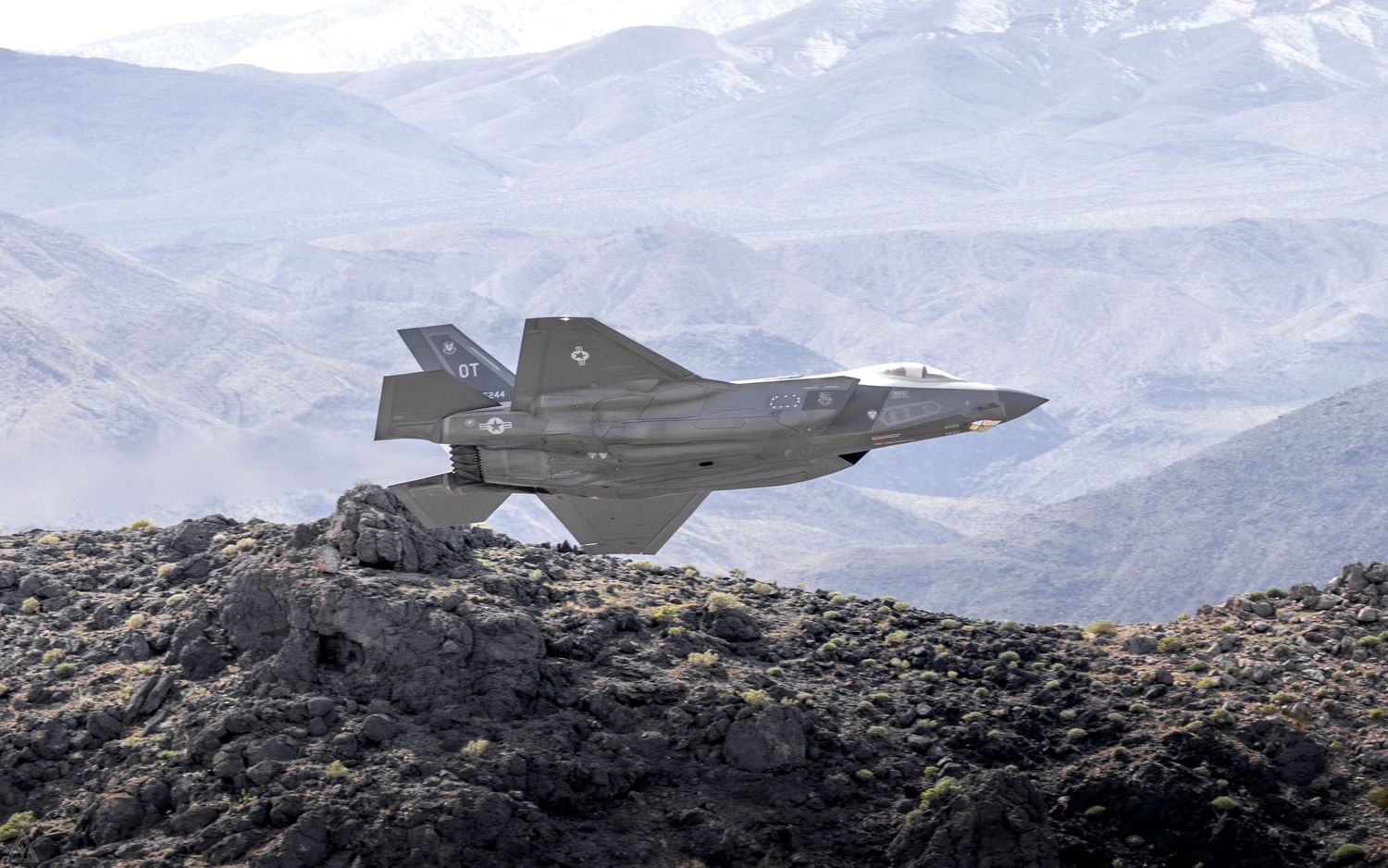 an F-35A flies at low level just above a desert mountain range