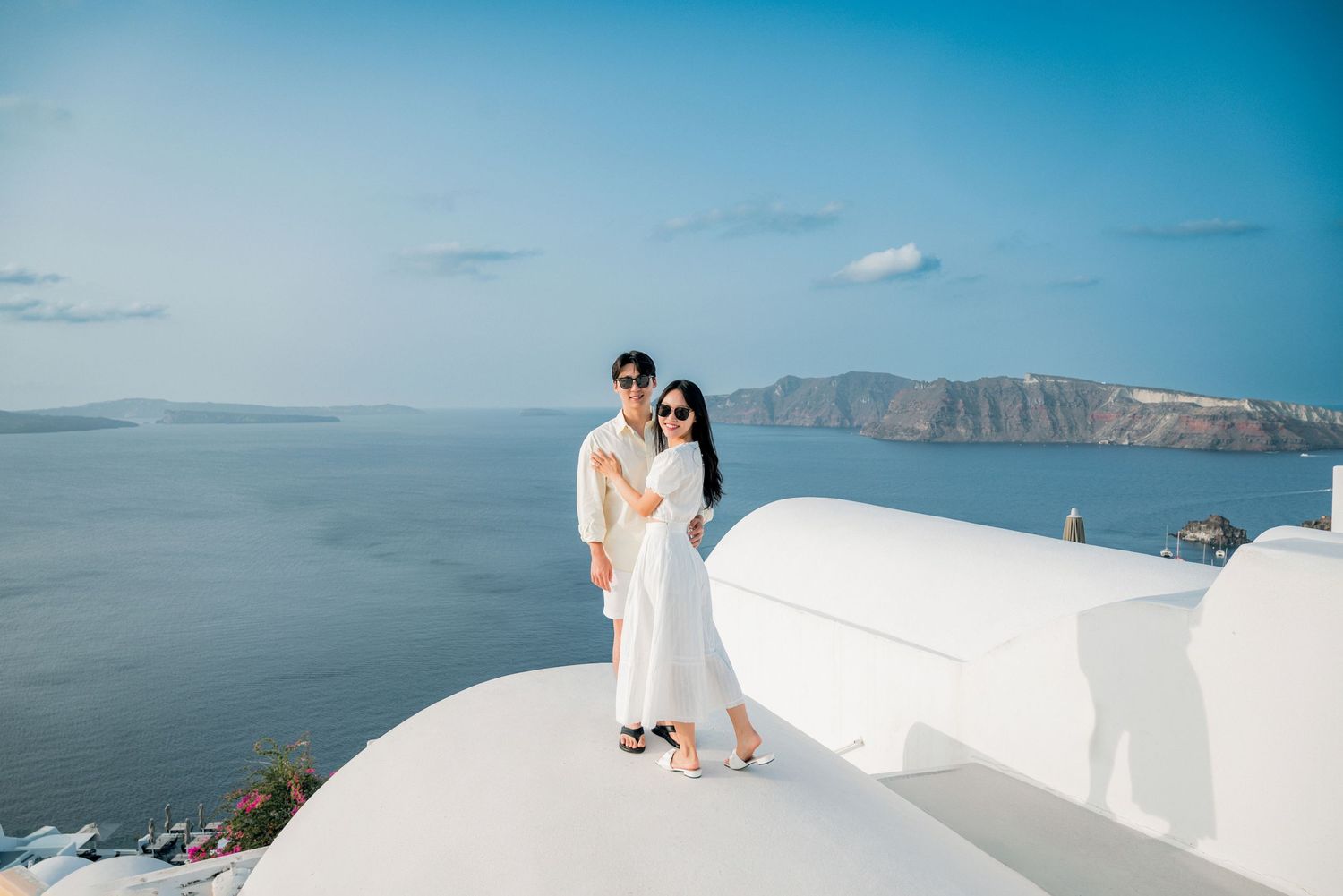 A blue-domed church in Santorini, Greece with white buildings and stunning caldera views over the Aegean Sea.
