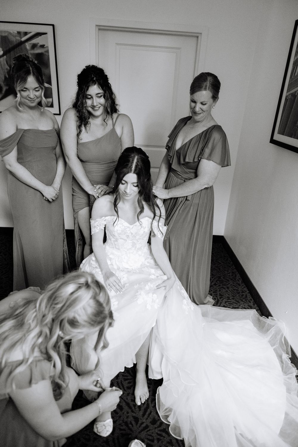 Black and white photo of wedding party helping with the bride's dress during preparation.