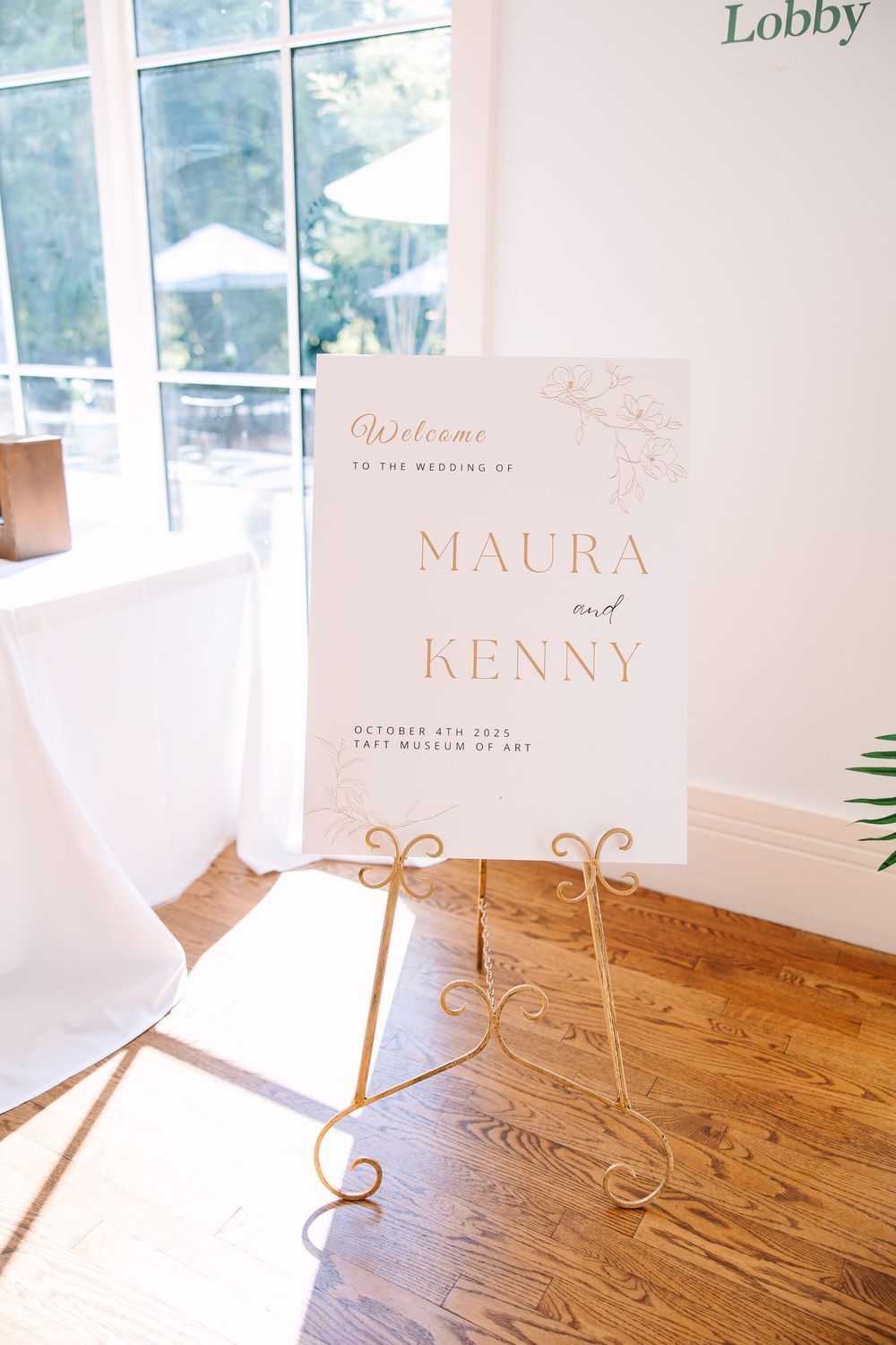 Wedding signage with names displayed on white paper stands against a wooden surface in an elegant lobby setting.