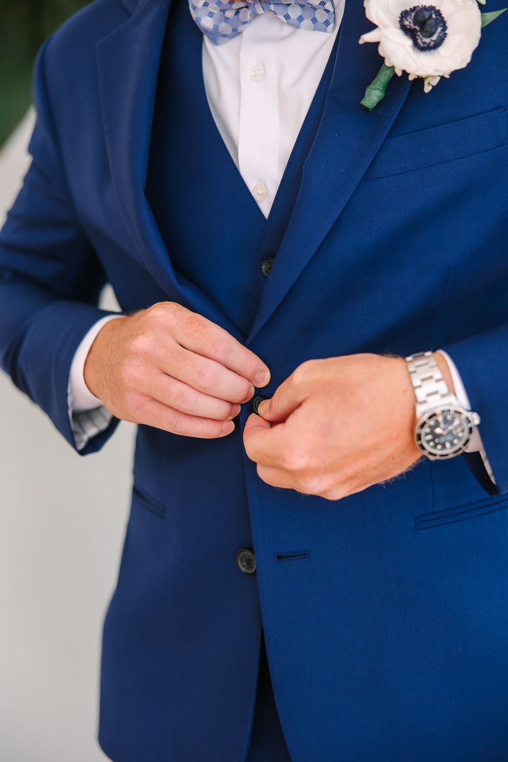 Close-up of a navy blue suit jacket with boutonniere and silver watch details.