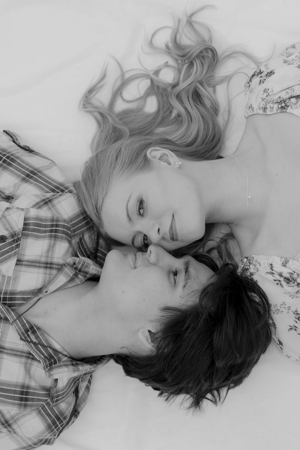 The image shows two young women lying together, one with long blonde hair and the other with dark hair, in a black and white photograph.