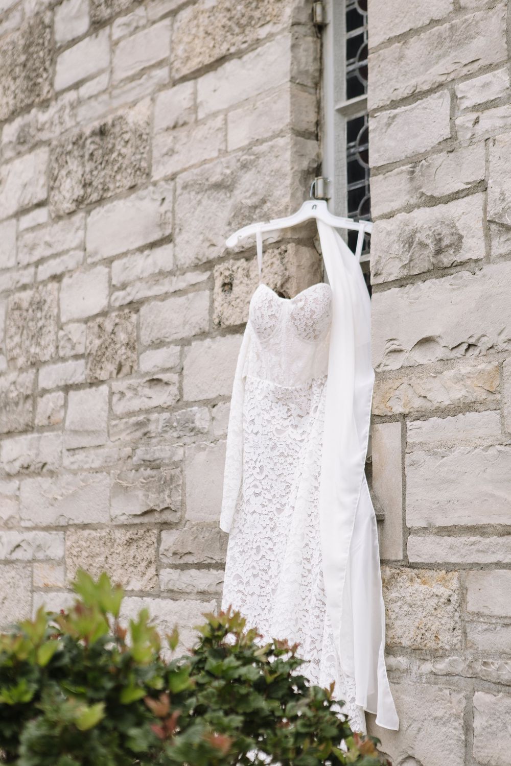 White lace dresses hanging on stone wall beside green shrubs and garden plants.
