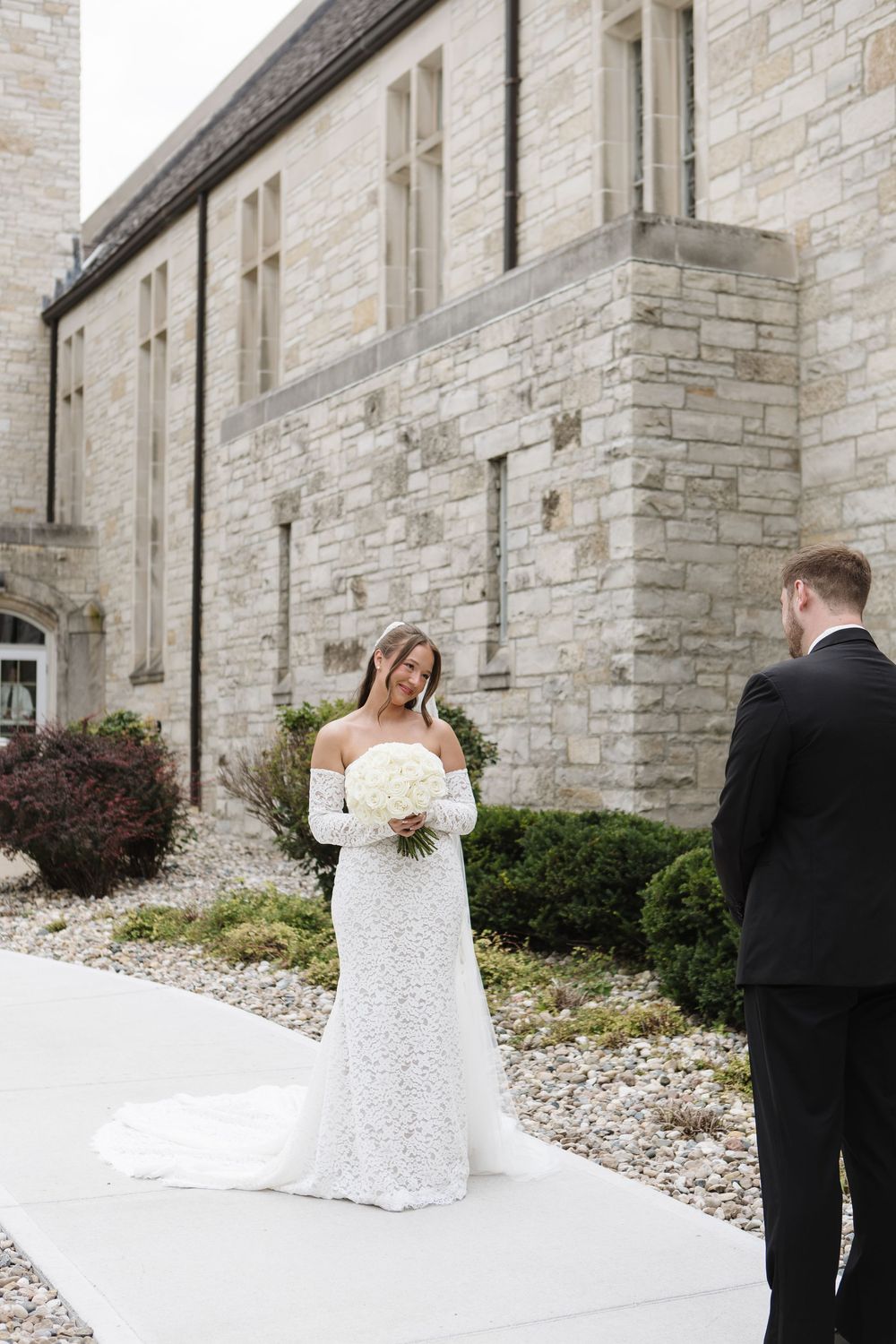 A bride and groom share a romantic first look moment outside a stone church building on their wedding day.