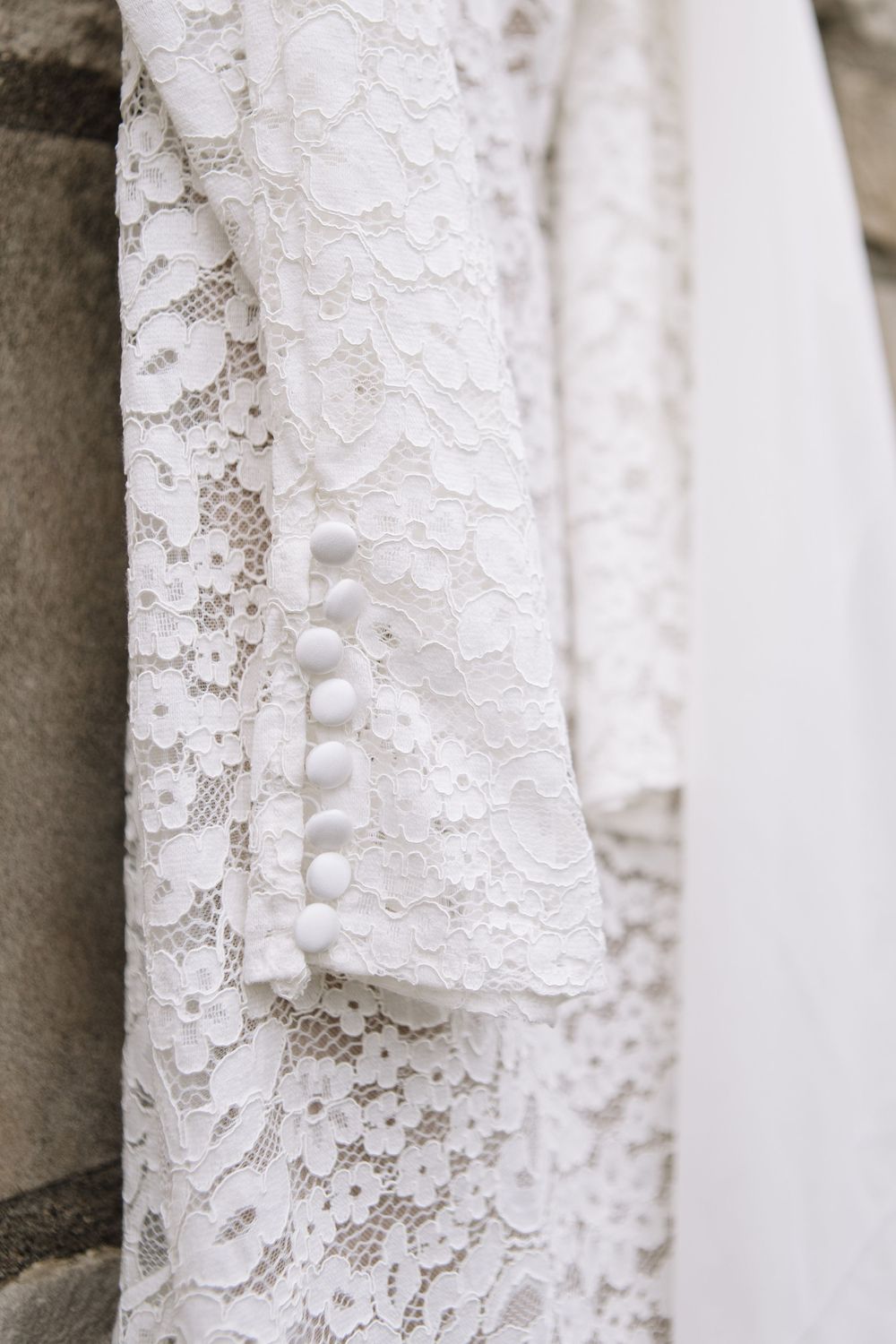 Close-up detail of delicate white lace fabric with button closures showing intricate floral patterns and textures.