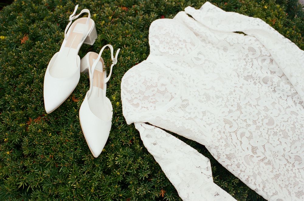 Close-up details of an intricate lace wedding dress against a garden background.