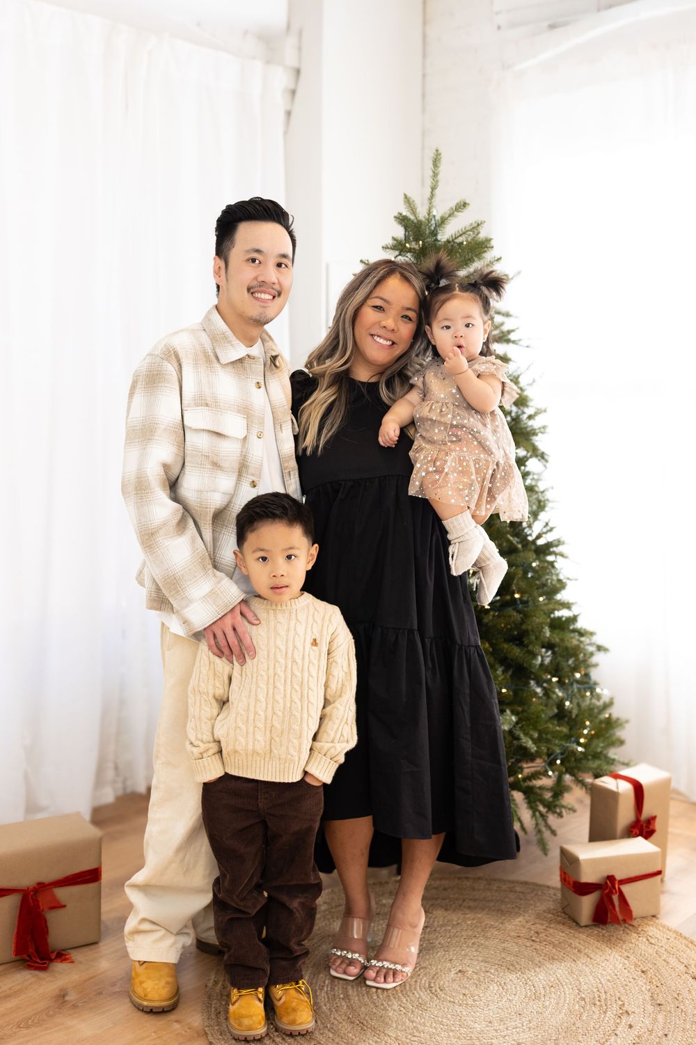 A family poses together in front of a decorated Christmas tree with wrapped presents beneath.