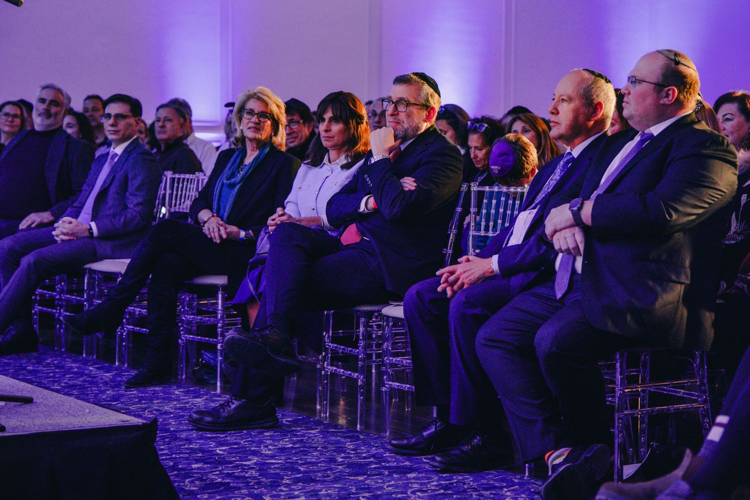 Conference attendees seated in rows at a venue illuminated with purple lighting during a professional event.