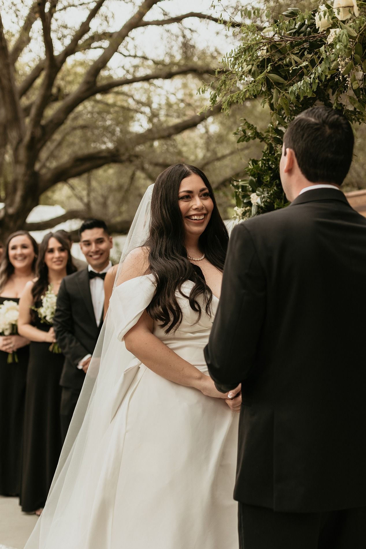 A wedding party gathers outdoors under large trees during a joyful celebration at The Oaks at Duncan Lane.