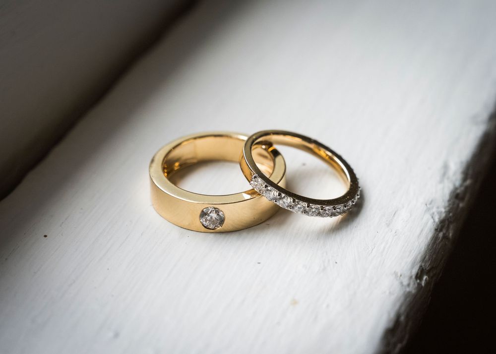 Two gold wedding rings with diamond accents resting on a white surface, symbolizing love and commitment.