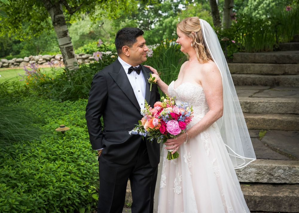 Bride and groom share romantic moment on garden steps, bride holding vibrant bouquet.