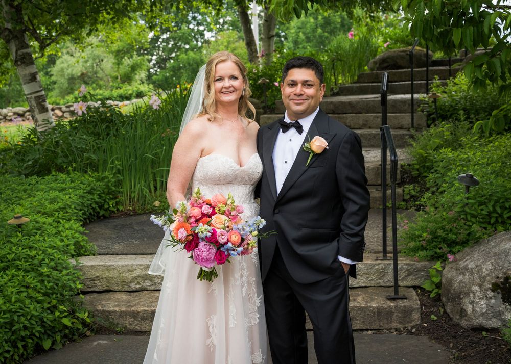 Bride and groom stand together in garden, bride holding vibrant bouquet in wedding attire.