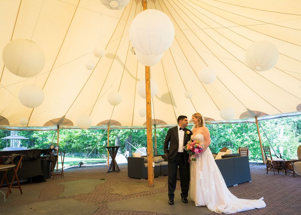 Bride and groom share a romantic moment under a white tent decorated with paper lantern lights at their outdoor wedding reception.