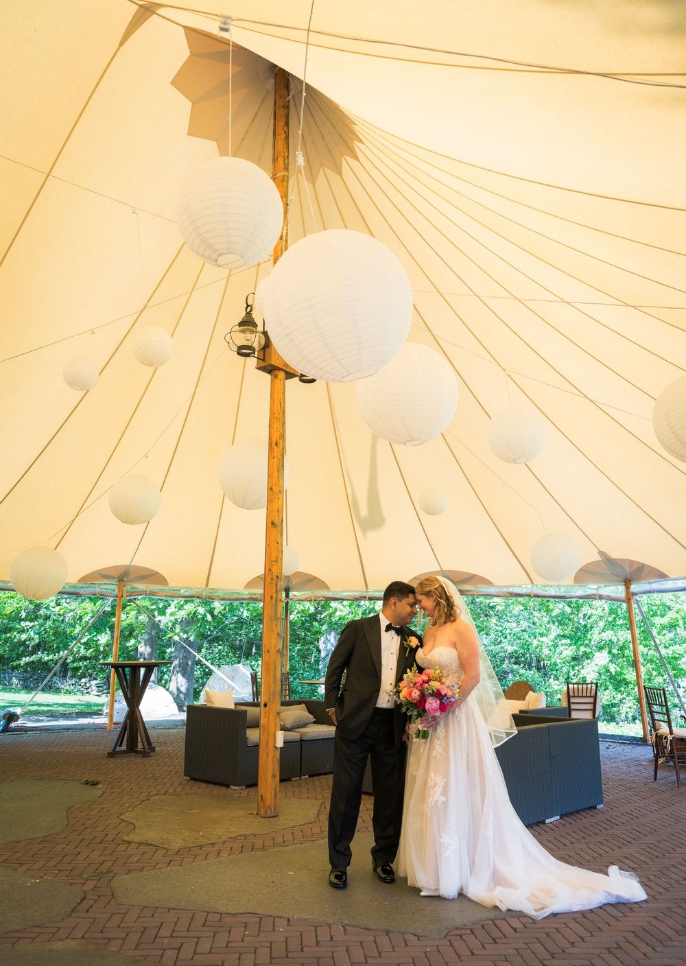 Bride and groom stand beneath elegant white tent decorated with paper lantern spheres at wedding reception.