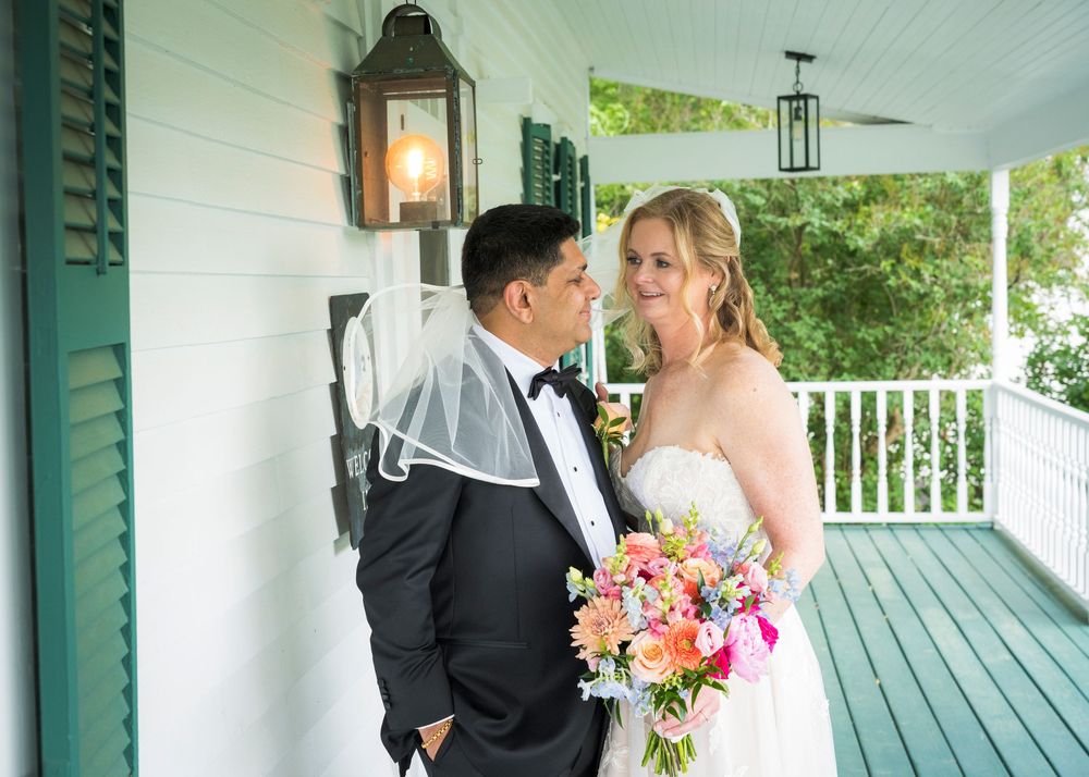 Bride and groom share a romantic moment on a white porch, bride holding colorful bouquet.