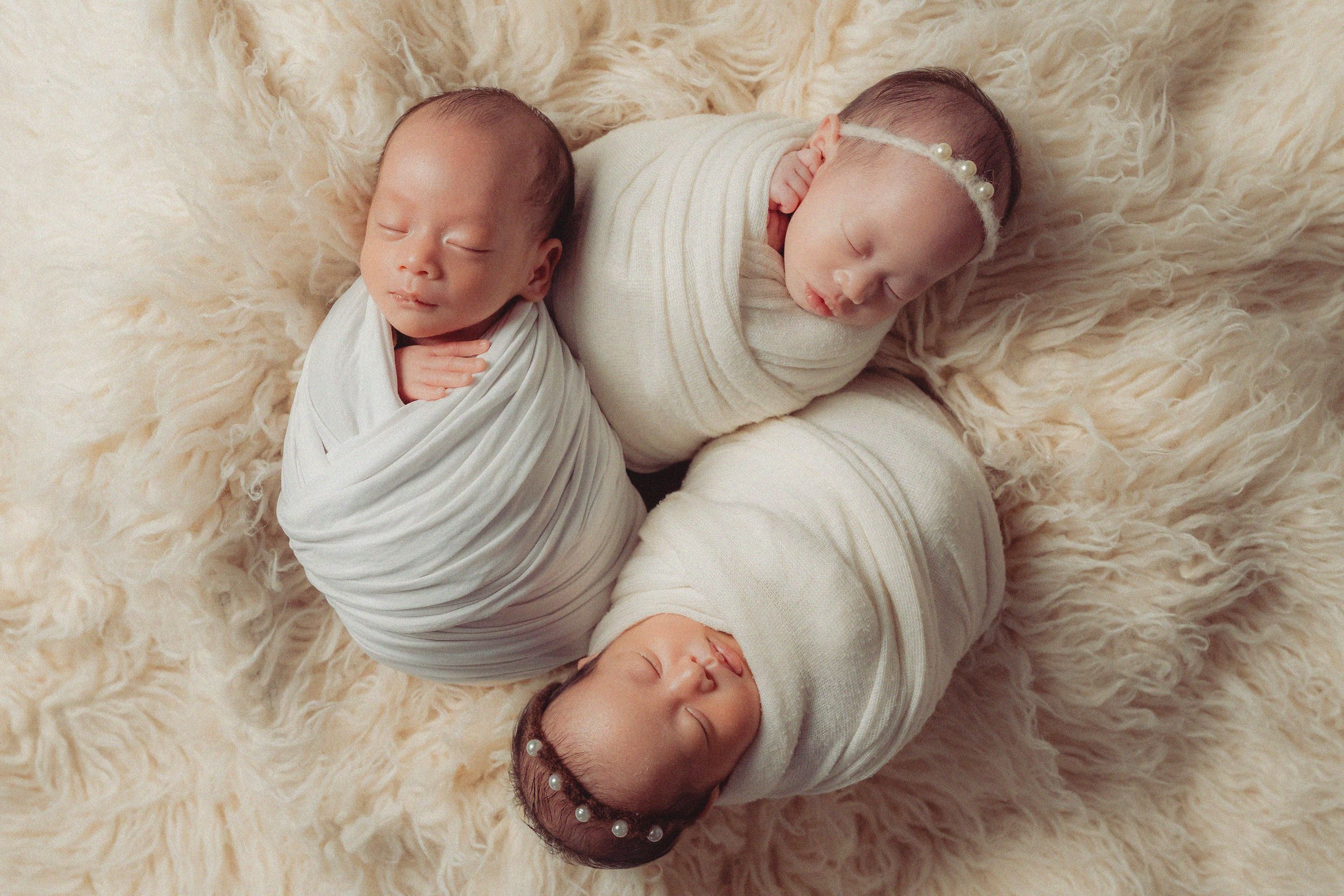 Collage of five sleeping newborn babies wrapped in white swaddles lying on soft cream-colored fur blankets.