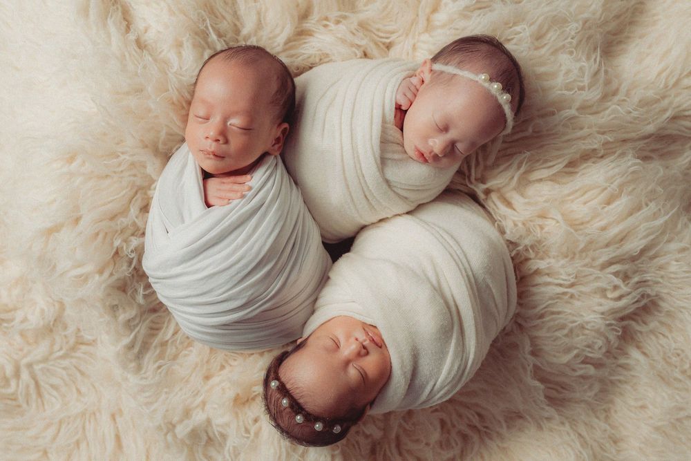 Collage of five sleeping newborn babies wrapped in white swaddles lying on soft cream-colored fur blankets.
