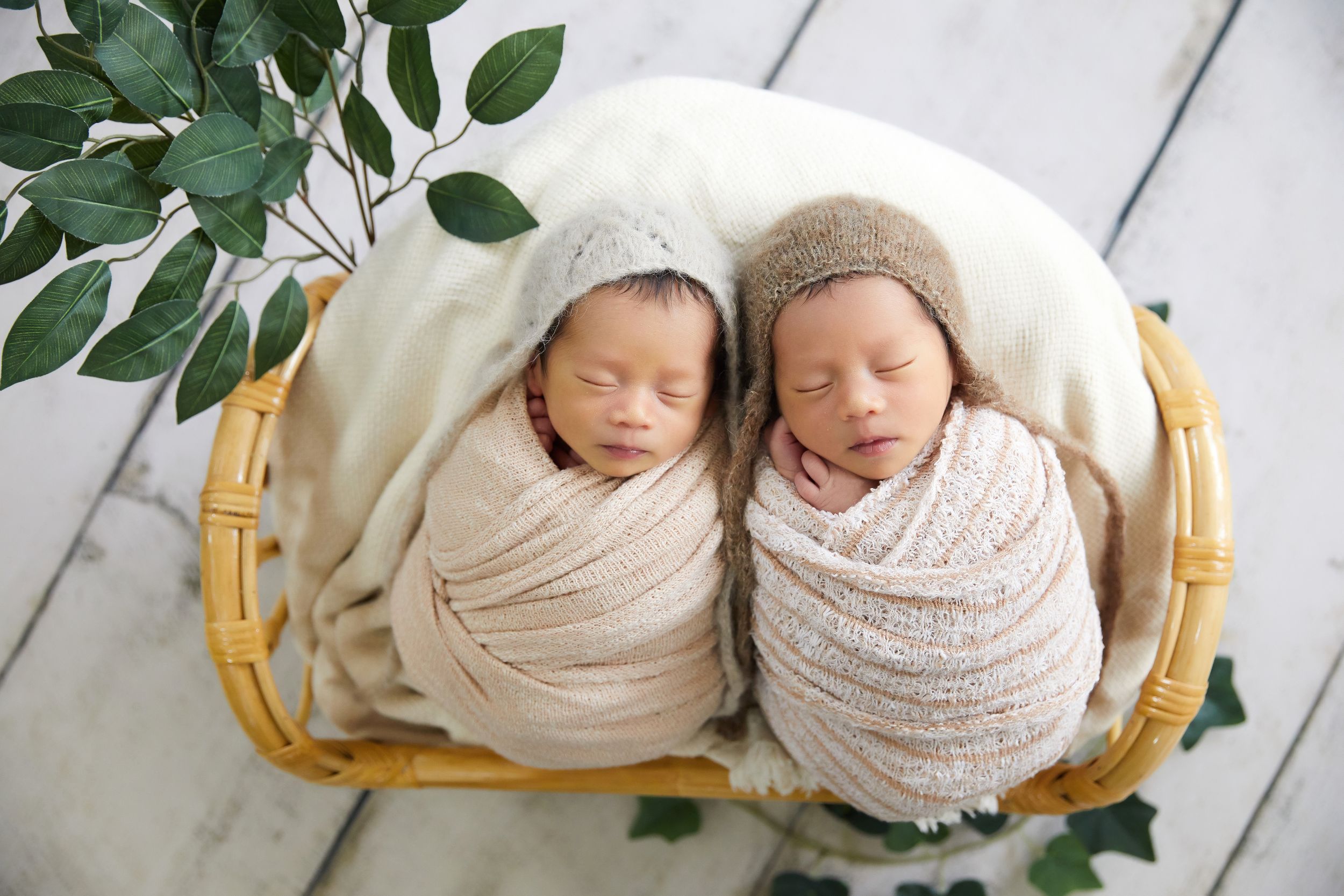 Two sleeping infants wearing cozy knit hats lie close together on a white wooden surface.