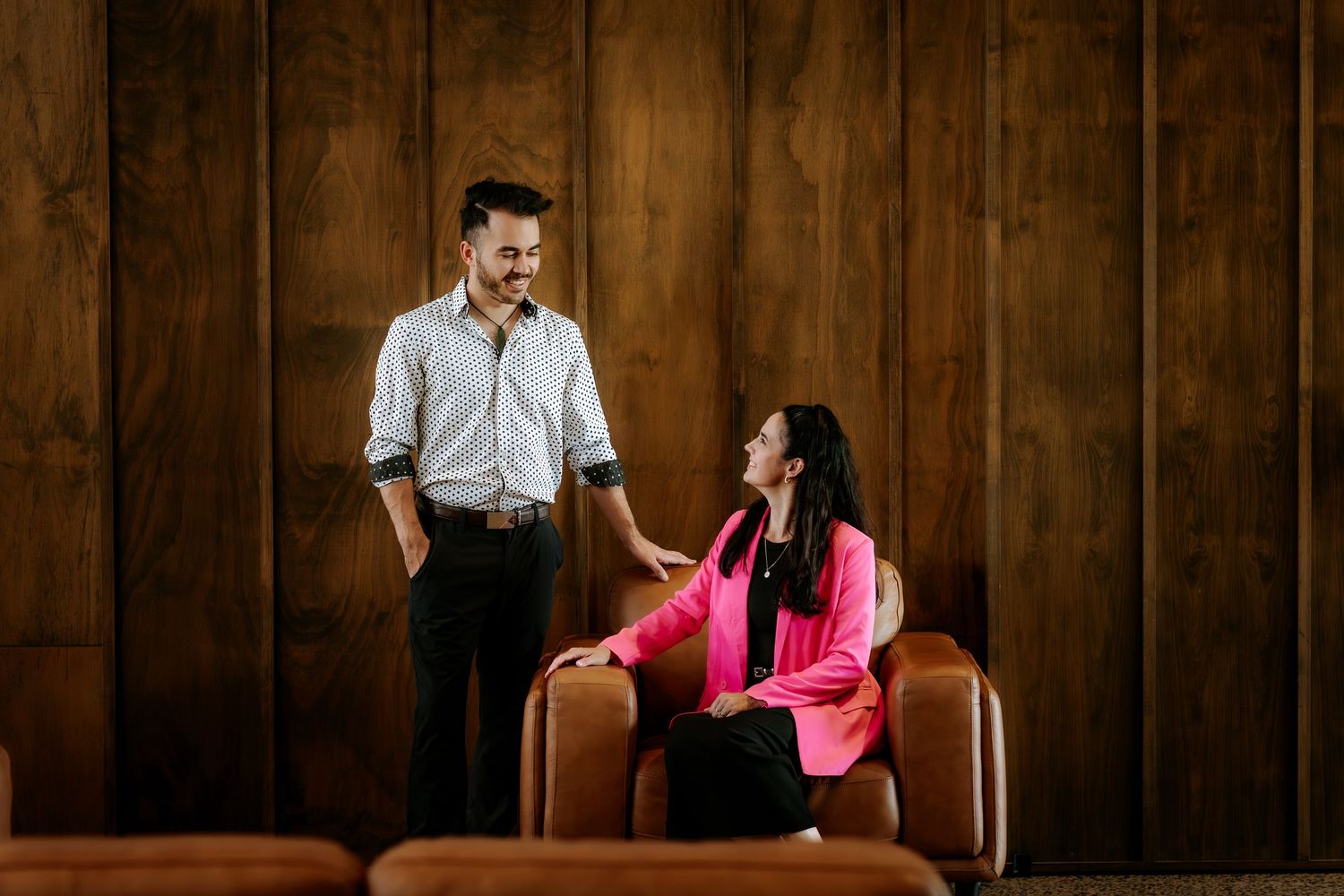 A couple shares a playful moment while standing against a rustic wooden wall.