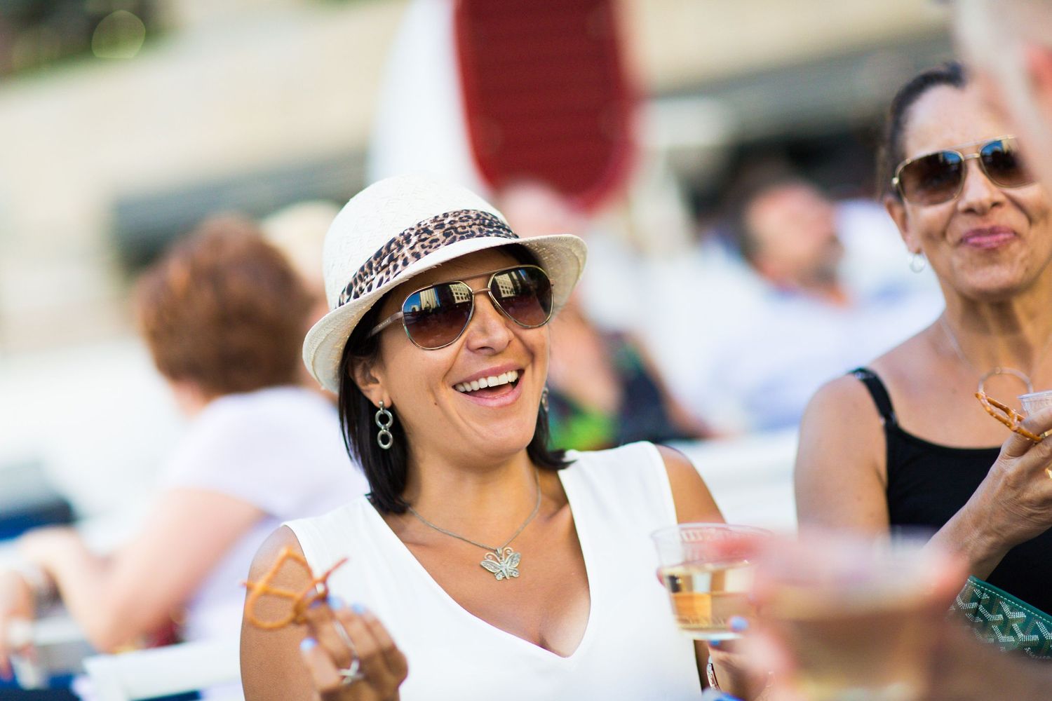 A woman in a white hat and sunglasses enjoying a drink at an outdoor social event.
