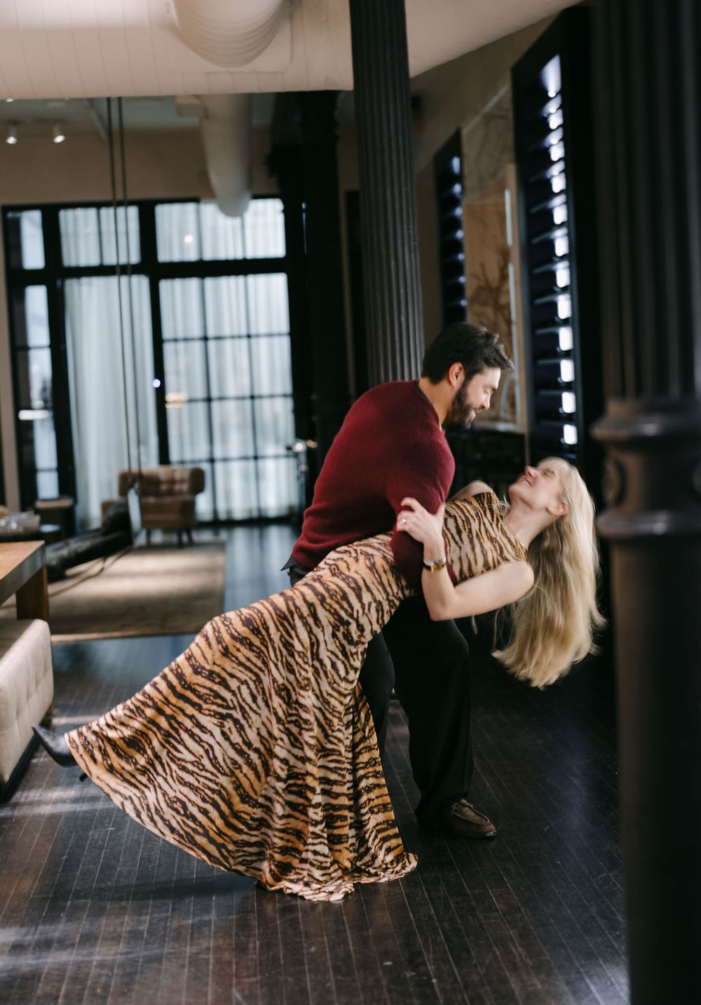A dramatic dance-like pose captured between two people in an industrial-style room with natural lighting.