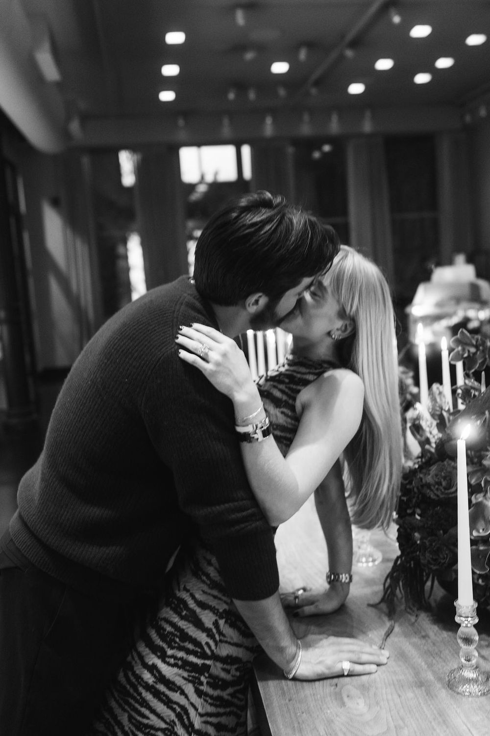 A black and white photo captures a tender kiss between a couple at an elegant candlelit setting.
