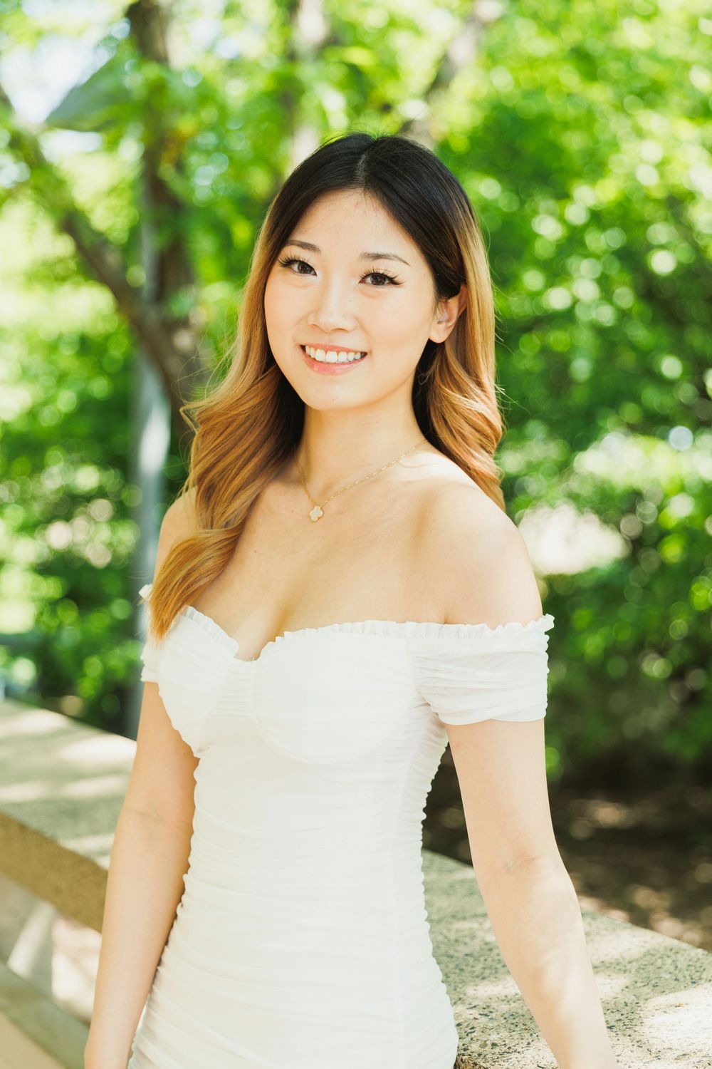 Outdoor portrait session in a white off-shoulder dress against lush green foliage.