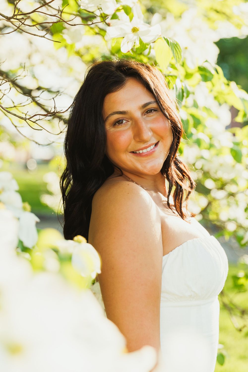 Portrait in a white dress against blooming spring flowers and sunlit foliage.