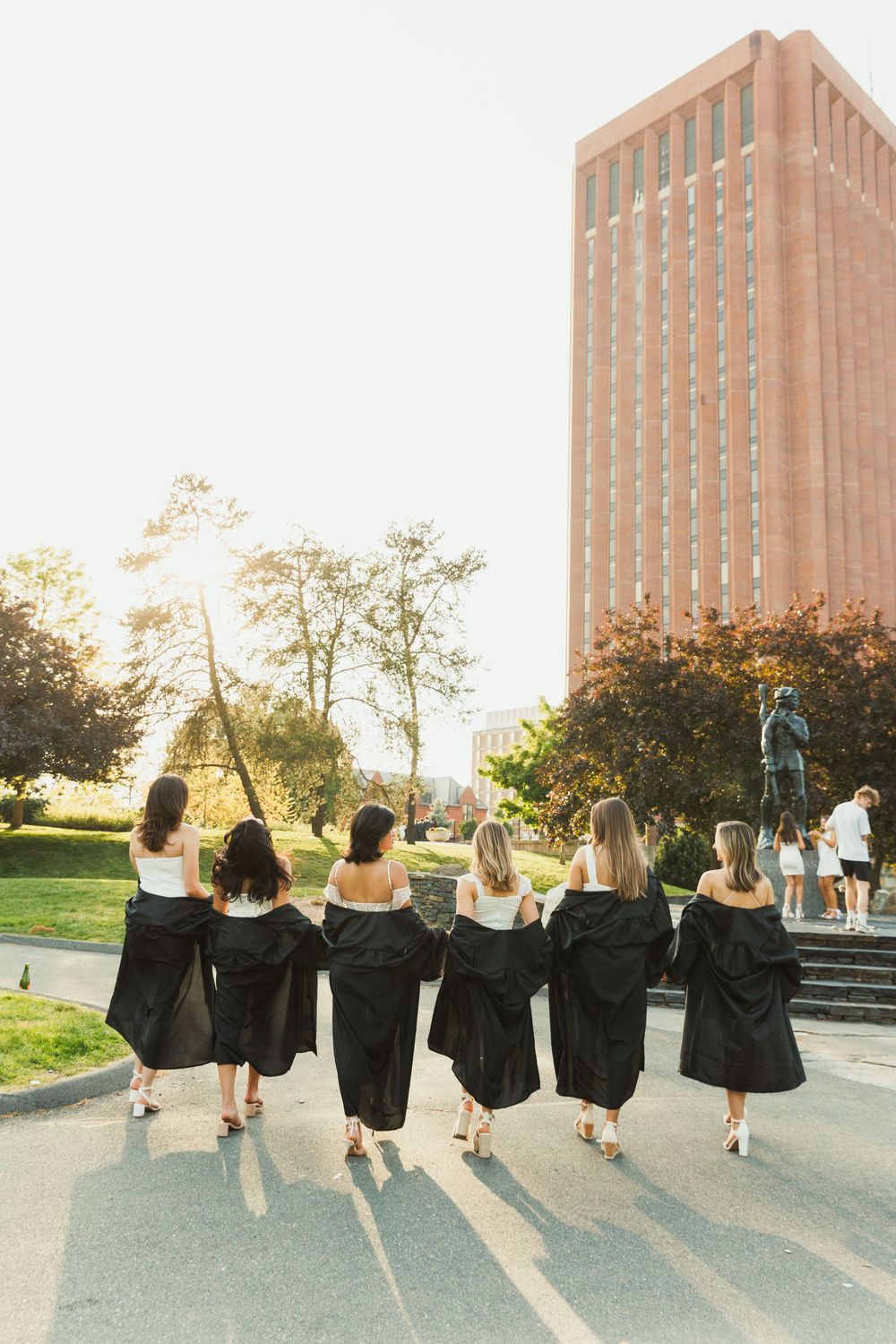 Group of graduates jumping in celebration while wearing black graduation gowns against a brick building.
