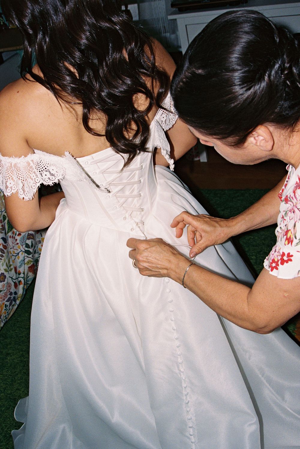 Helper lacing up the back of a brides white corset wedding dress before the ceremony.