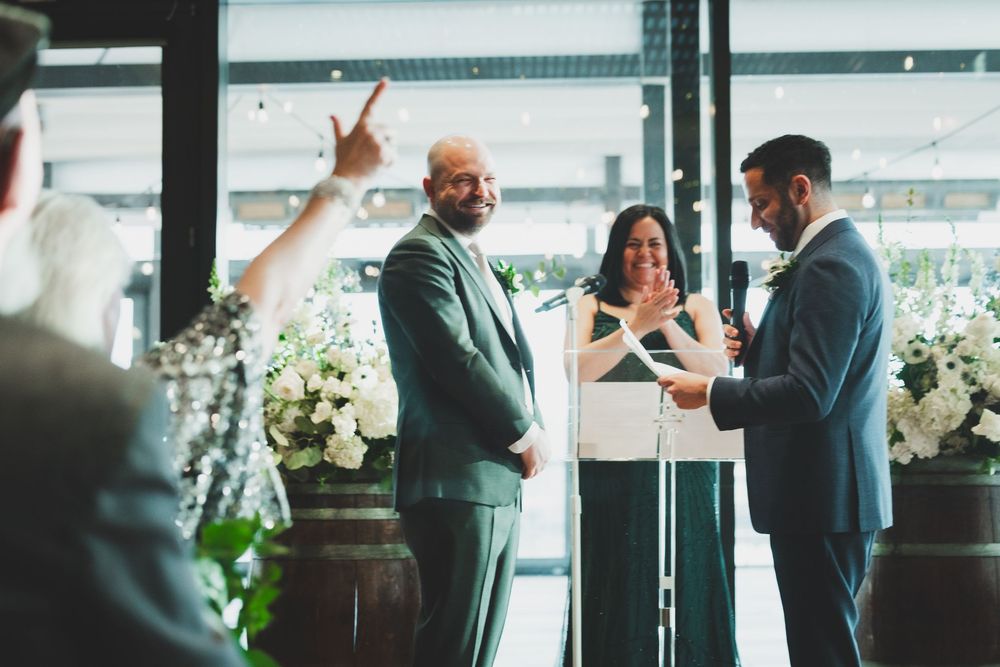 A joyful wedding ceremony takes place in a bright venue called district winery dc, decorated with white floral arrangements.
