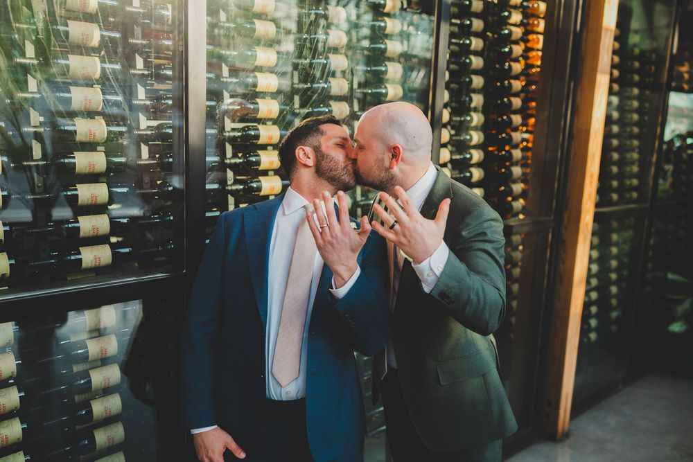 Two people share an intimate moment in a wine cellar surrounded by illuminated wine bottle displays.