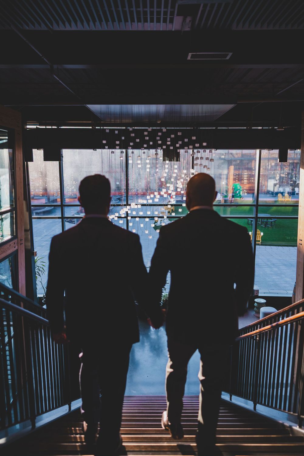 Two silhouetted figures stand at a railing overlooking a cityscape in a moody, cinematic composition.