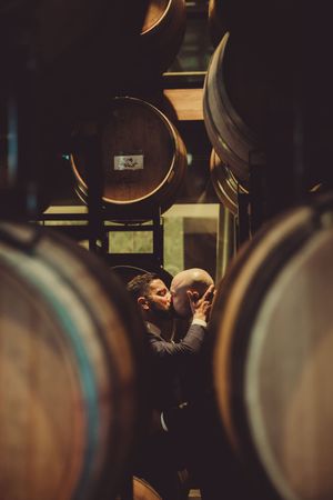 Two grooms kissing in a dark cellar surrounded by wooden barrels at the district winery dc.