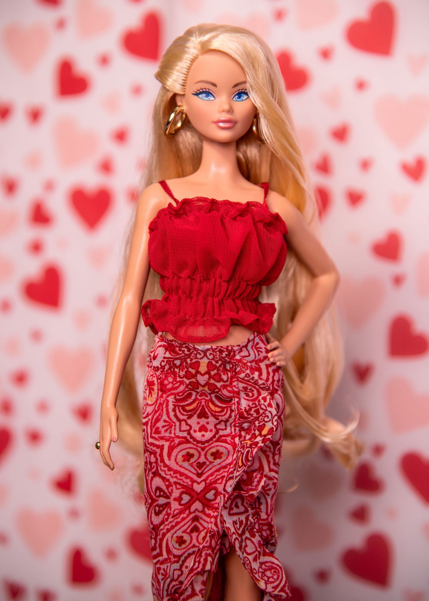 Blonde Barbie doll styled in red ruffle top and red patterned skirt with heart-print backdrop.