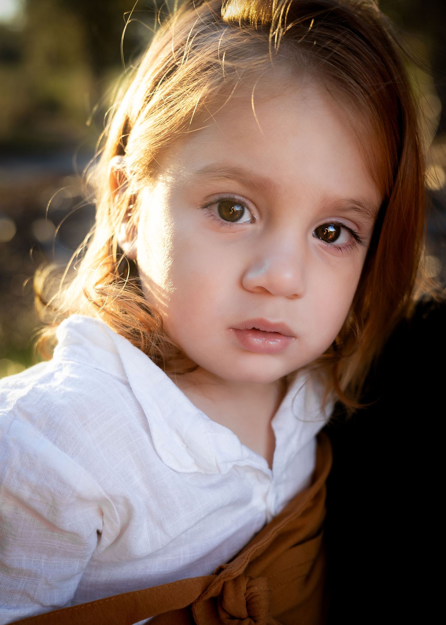 A young child in a white collared shirt looking off to the side with soft lighting and a blurred background.