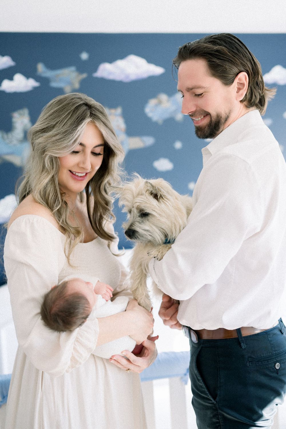 A couple poses with their small white dog and newborn baby at their in home newborn session in Washington DC