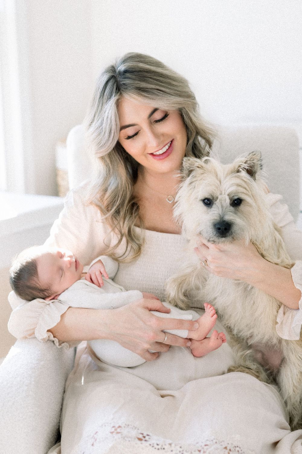 A tender moment captured as a small white dog sits beside a sleeping baby on a cozy white chair at a newborn session in washington dc