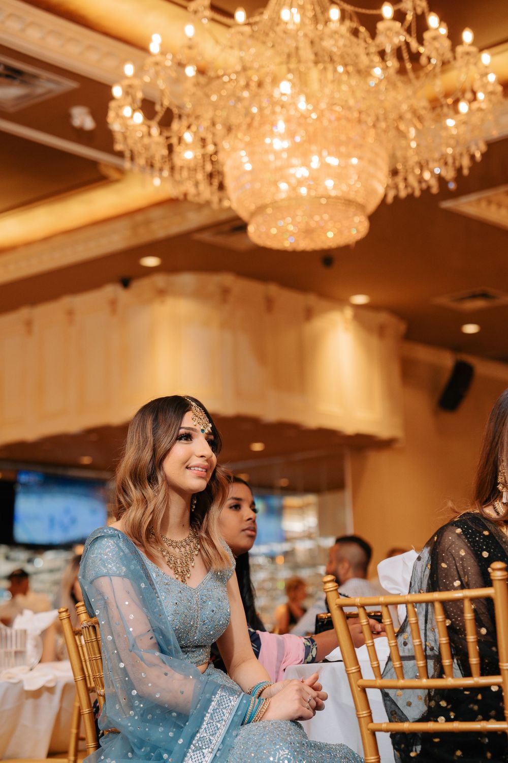 Guests seated at elegant tables under crystal chandeliers during an upscale event in a luxurious ballroom.