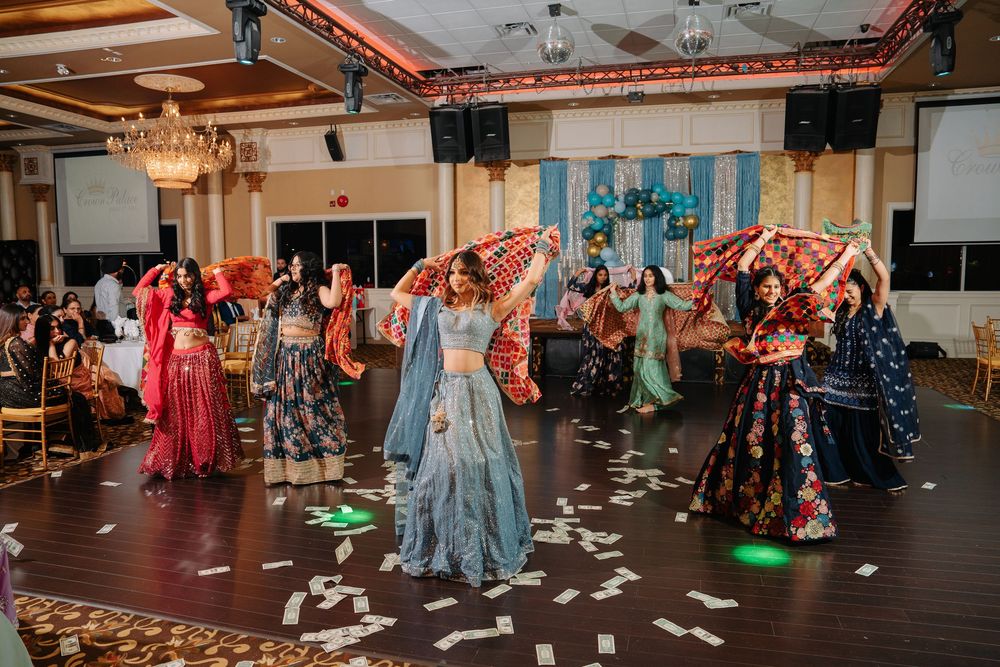 Wedding reception guests dance and celebrate on a wooden dance floor under elegant chandeliers in a ballroom setting.