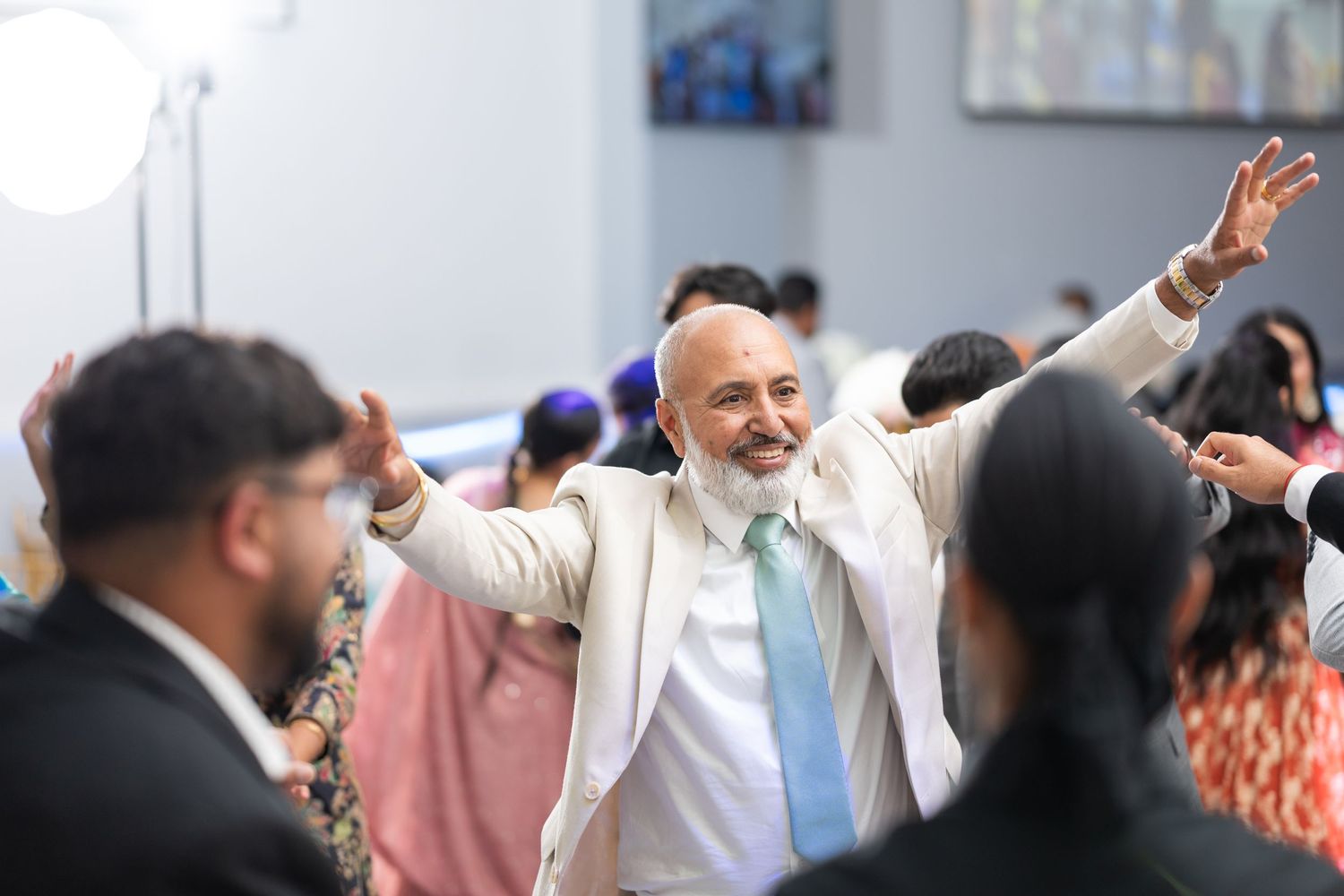 People dancing and celebrating at an outdoor wedding reception with arms raised in joyful motion.