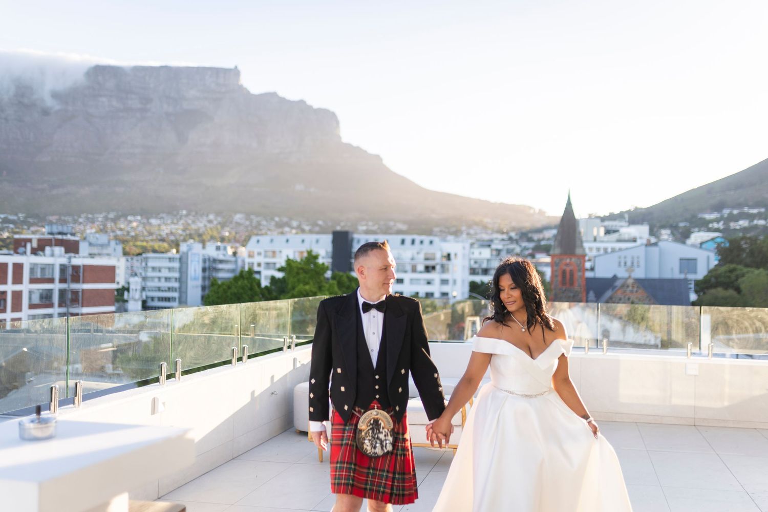 Bride and groom holding hands on rooftop terrace with Table Mountain backdrop in Cape Town, South Africa.